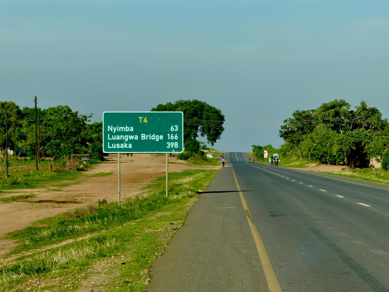 A green road sign on a straight highway displaying distances to Nyimba and Lusaka, symbolizing the concept of vector magnitude and geometric norm.