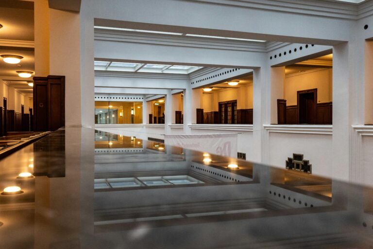 A high-angle interior shot of white architectural beams and pillars reflecting on a polished floor, creating a series of parallel and redundant geometric lines like linear dependent set in linear algebra.