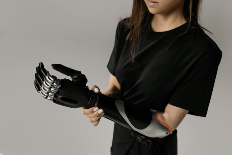A side view of a person wearing a high-tech black and silver prosthetic arm against a plain gray background.