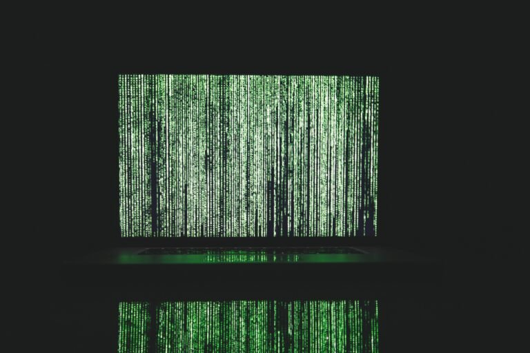 A laptop screen displaying cascading vertical lines of green digital code in a dark room, reflecting off the surface below, evoking a mathematical matrix theme.
